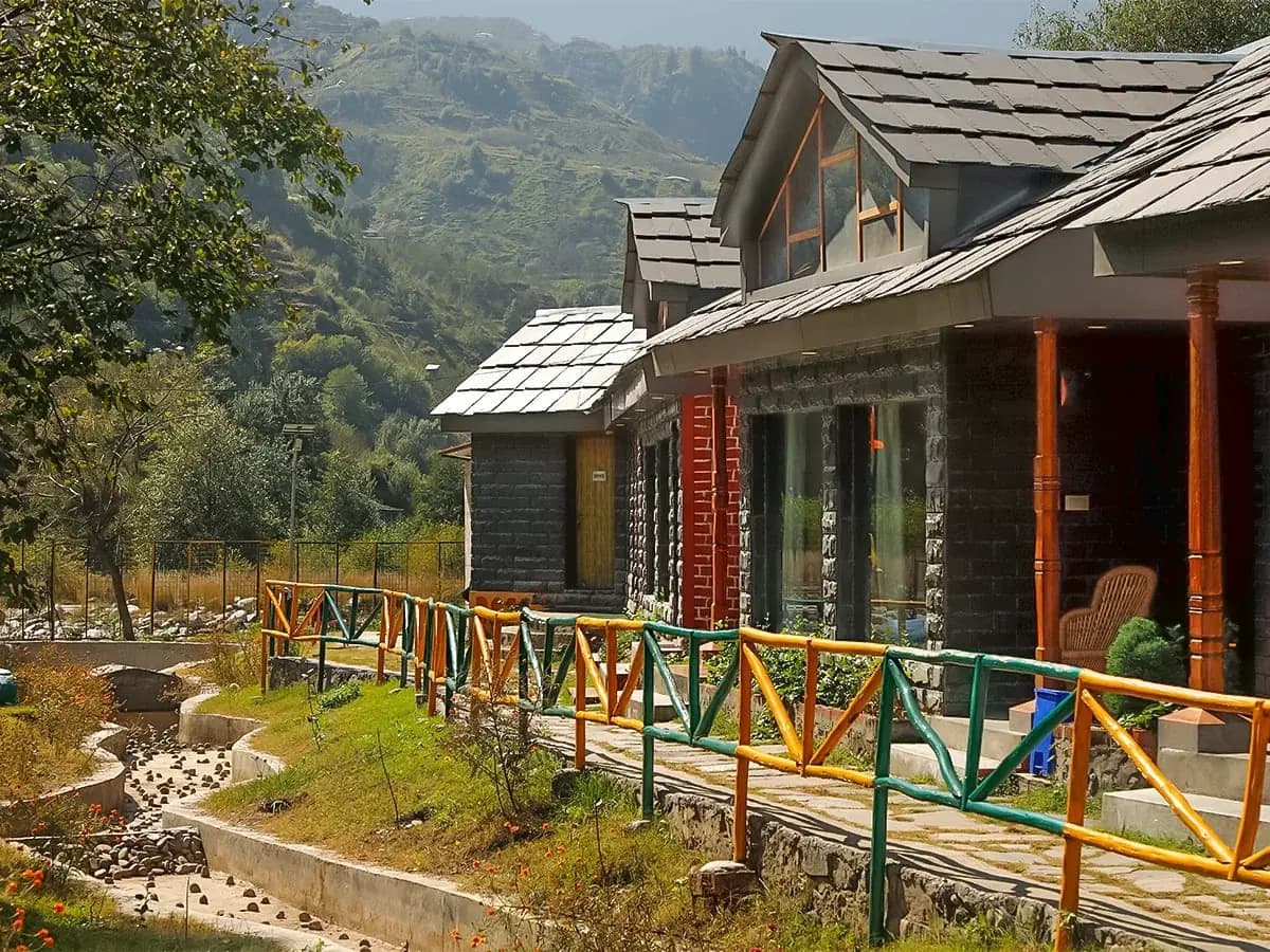 Stone-and-slate cottages at Chanshal Camps & Resort beside a stream